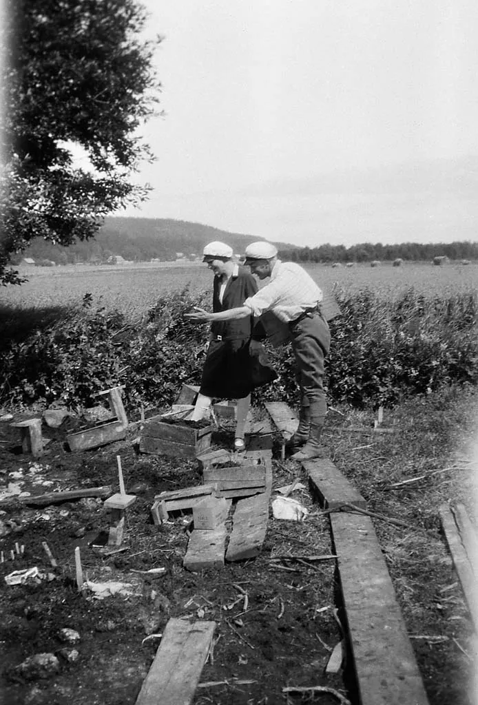 Arkeologen Holger Arbman visar Berit Wallenberg utgrävningen av Alvastra pålbyggnad 1928 (Riksantikvarieämbetet). Den vattenmättade torven har bevarat pålar av ek och alm, stockgolv, härdar, äpplen och sädeskorn från omkring 3000 f.Kr.