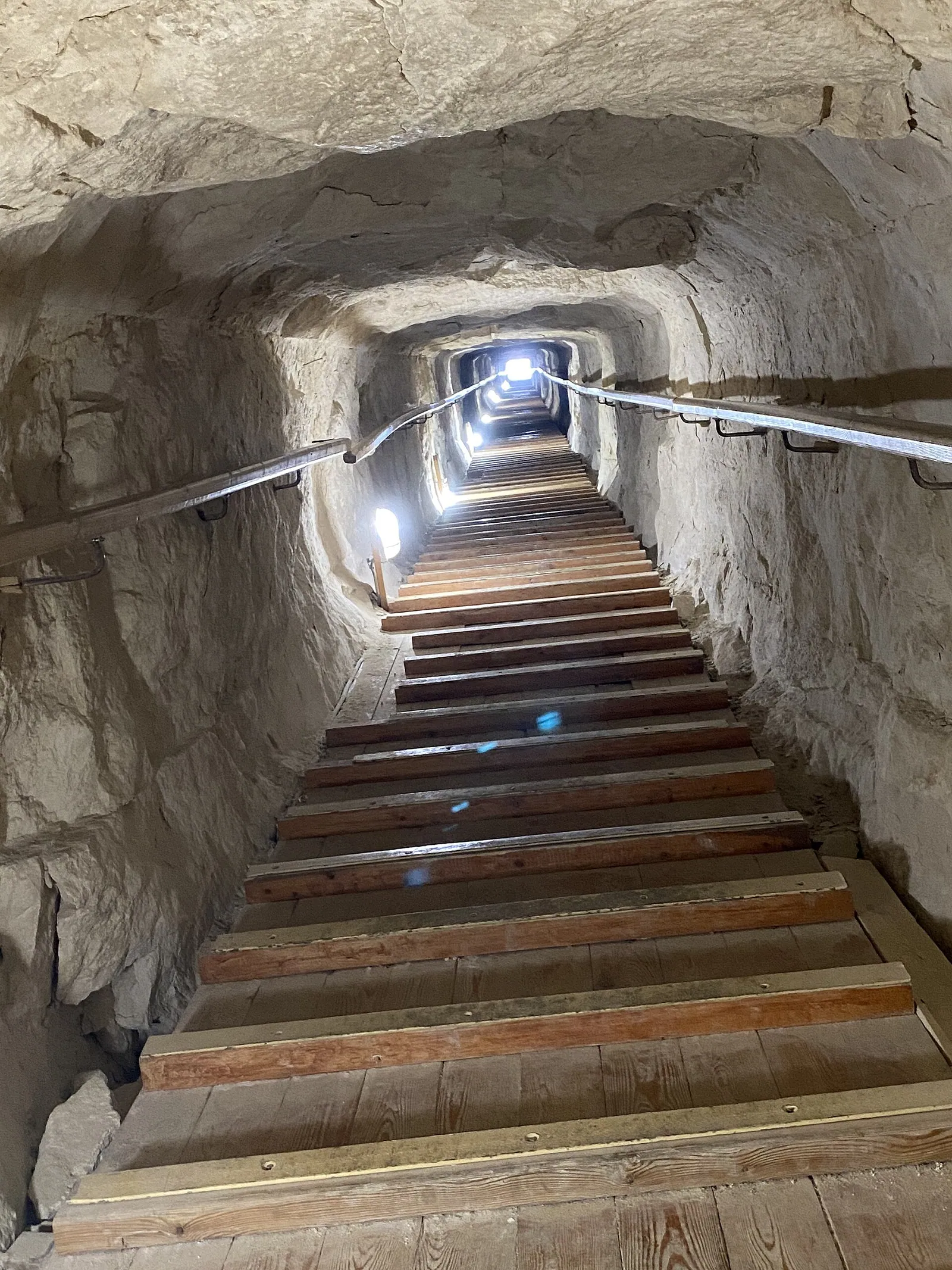 Halvvägs ned i Knäckta pyramidens omkring 79 meter långa norra gång, med blicken tillbaka mot ingången. Den är bara ungefär 1,1 meter hög och bred, och trästegen sattes in inför återöppningen 2019. Ungefär 12,6 meter in kan ni känna efter det 23 centimeter höga steget där den yttre delen har satt sig.