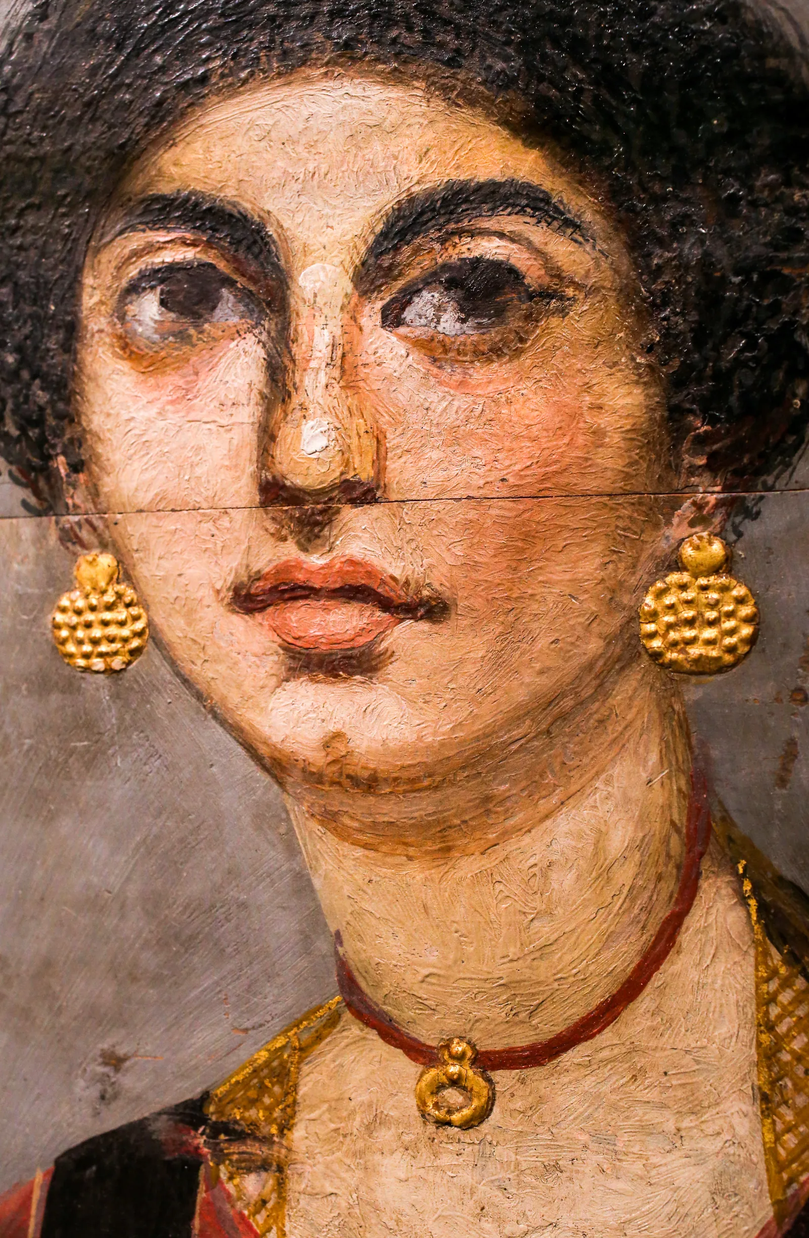 Porträtt av en ung kvinna från Hawara, enkaustik på trä, tidig flavisk tid (slutet av 1:a århundradet e.Kr.; Ägyptisches Museum, Berlin, ÄM 10974): lockigt hår, tegelröd tunika, örhängen med guldskivor och ett månskäreformat hänge.