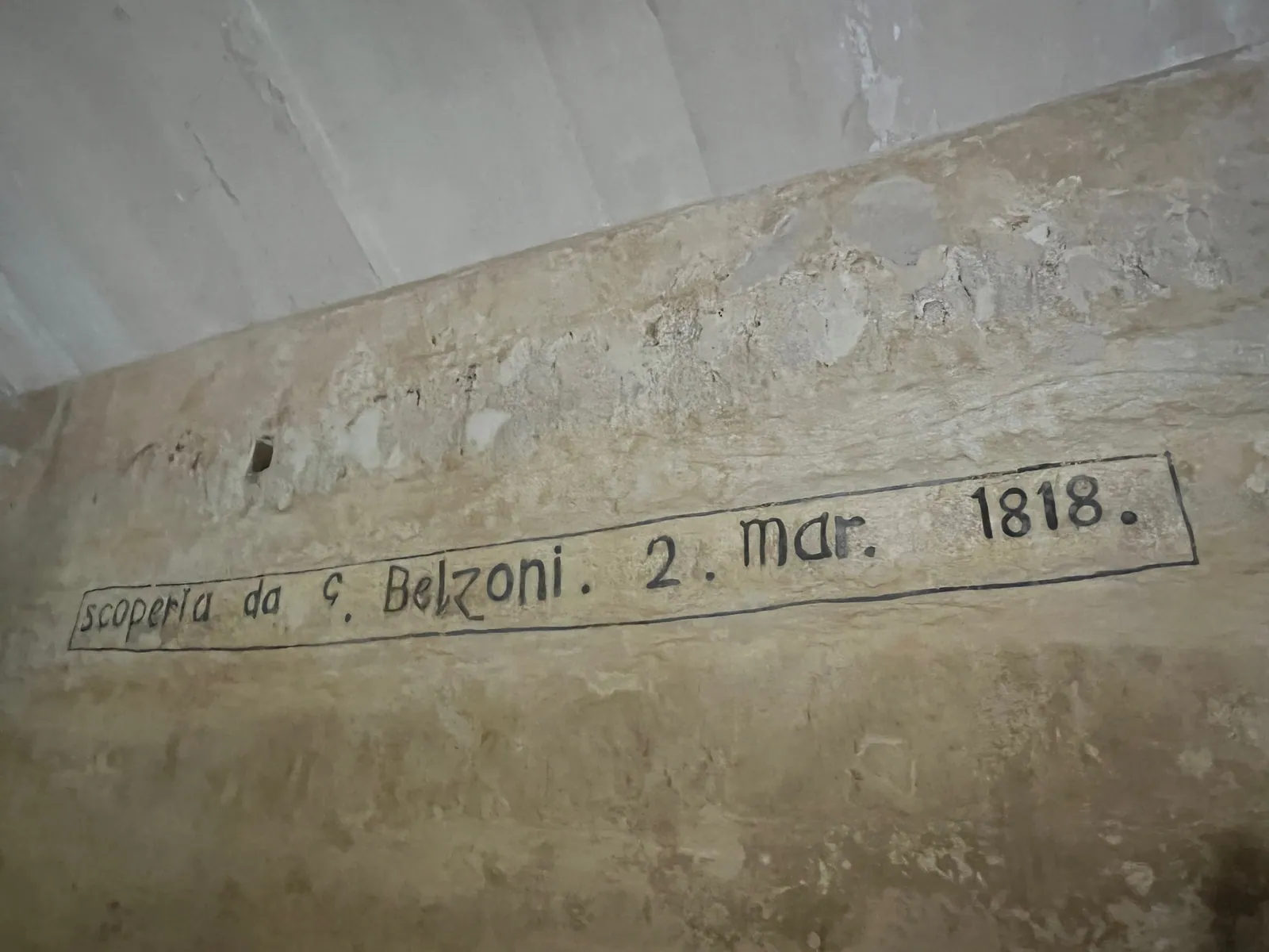 'Scoperta da G. Belzoni. 2. mar. 1818.' ('Upptäckt av G. Belzoni den 2 mars 1818'), målat med stora svarta bokstäver på sydväggen i Khafres gravkammare, fotograferat 2022. Leta upp texten dag 7, och spana efter den arabiska inskrift som han skrev av från västväggen.