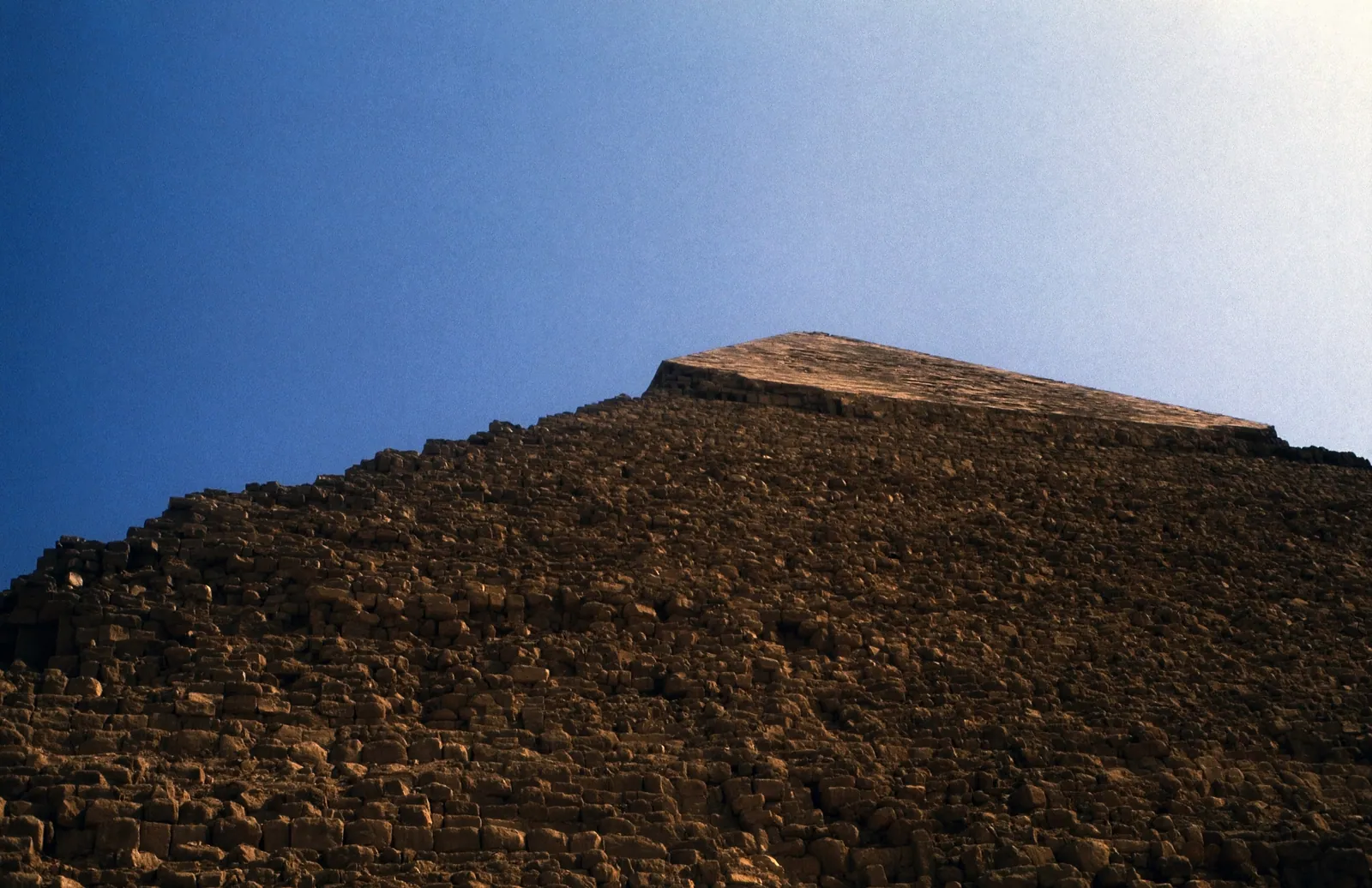 Blick uppför en av Khafrepyramidens sidor mot den bevarade kappan av slät kalkstensbeklädnad (1983). Under den syns den trappstegsformade kärnan där beklädnaden har plockats bort, dels till Ramses II:s byggen, dels senare till det medeltida Kairo.