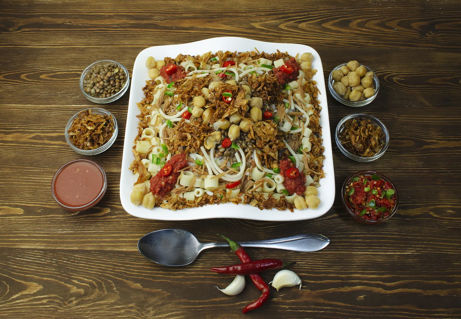 Koshari, Egyptens nationalrätt från gatuköket: ris, linser, makaroner och kikärtor under tomatsås och krispig rostad lök, med vitlöksvinäger och chili vid sidan.