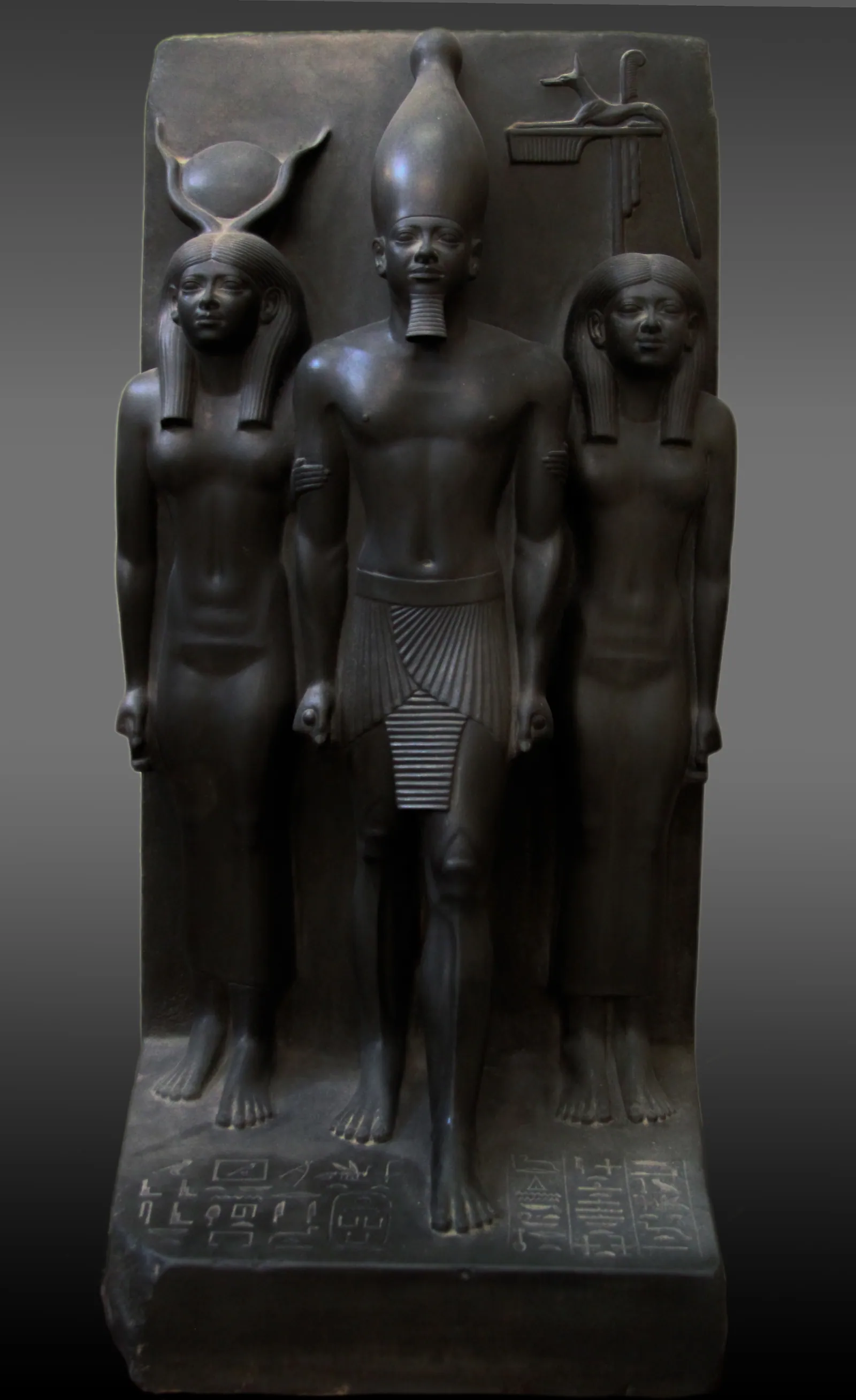 En av triaderna i gråvacka som Reisner hittade i Menkaures daltempel 1908: kungen med den vita kronan mellan Hathor och den personifierade 17:e (schakal-)provinsen i Övre Egypten (Egyptiska museet i Kairo, JE 40679; 92,5 cm).